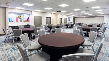 A conference room with multiple tables and chairs, a projector screen, and a carpeted floor.