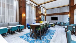 A hotel dining area with a long communal table, multiple chairs, and a sofa. - Hampton Inn & Suites Houston Heights I-10 (Houston)