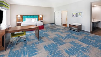 A hotel room with a bed, desk, chair, and a bathroom with a sink and mirror.