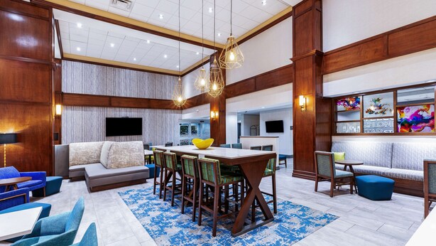 A spacious lobby with a central dining area, seating arrangements, and a large flat-screen TV. - Hampton Inn & Suites Houston Heights I-10 (Houston)