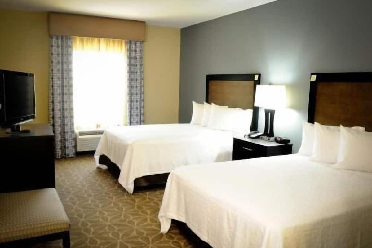 A hotel room with two beds, a television, a desk, and a lamp.