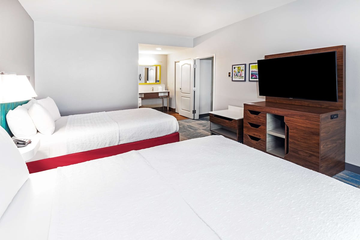 A hotel room with a bed, a TV, a desk, and a bathroom visible through an open door.