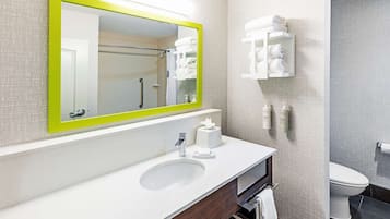 A modern bathroom with a white sink, a mirror with a green frame, a toilet, and a shower area.