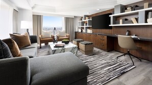 A modern living room with a sofa, coffee table, and ottoman, a kitchen area with wooden cabinets and a flat-screen TV, and a large window offering a city view. - Hyatt Regency San Francisco Downtown SOMA    (San Francisco)