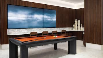 Une table de billard au design moderne, entourée de lambris en bois et agrémentée d’un grand téléviseur fixé au mur.