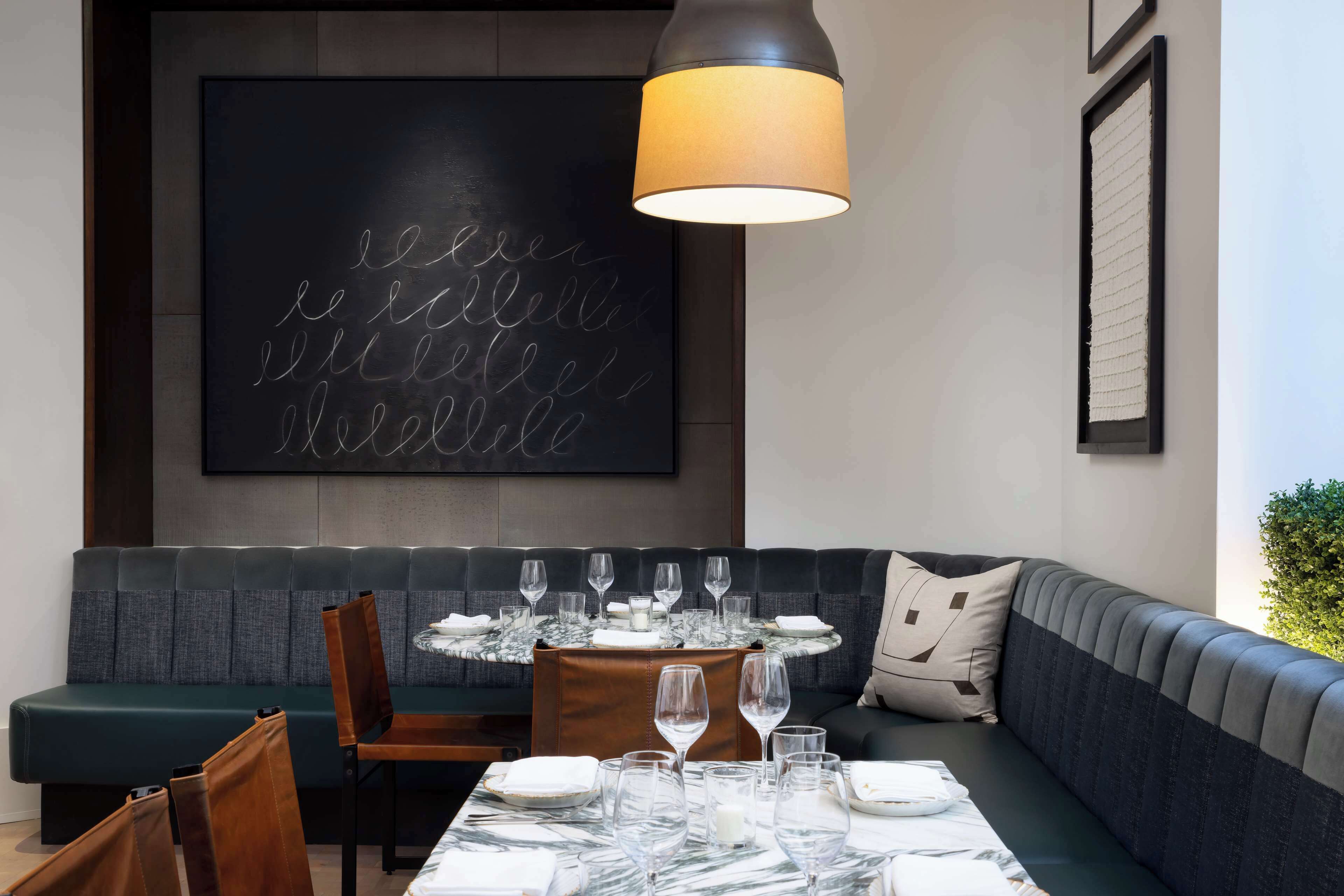 Un comedor moderno con una mesa de mármol preparada para seis comensales, un sofá verde oscuro y una pizarra grande con texto.