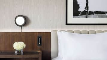 Une chambre d’hôtel avec une tête de lit en bois, une table de chevet ornée d’un vase de fleurs, un tableau encadré au mur et un lit avec une literie blanche.