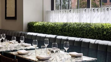 Un restaurante con una larga mesa de comedor lista para una comida, un banco acolchado y una ventana con persianas.