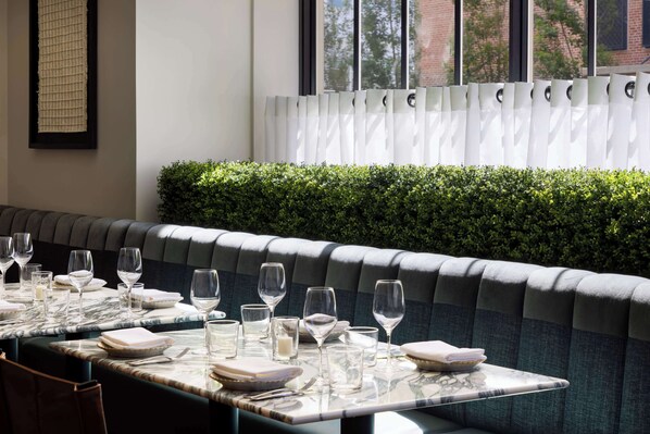 A restaurant with a long dining table set for a meal, a cushioned bench, and a window with blinds. - Hyatt Regency San Francisco Downtown SOMA    (San Francisco)
