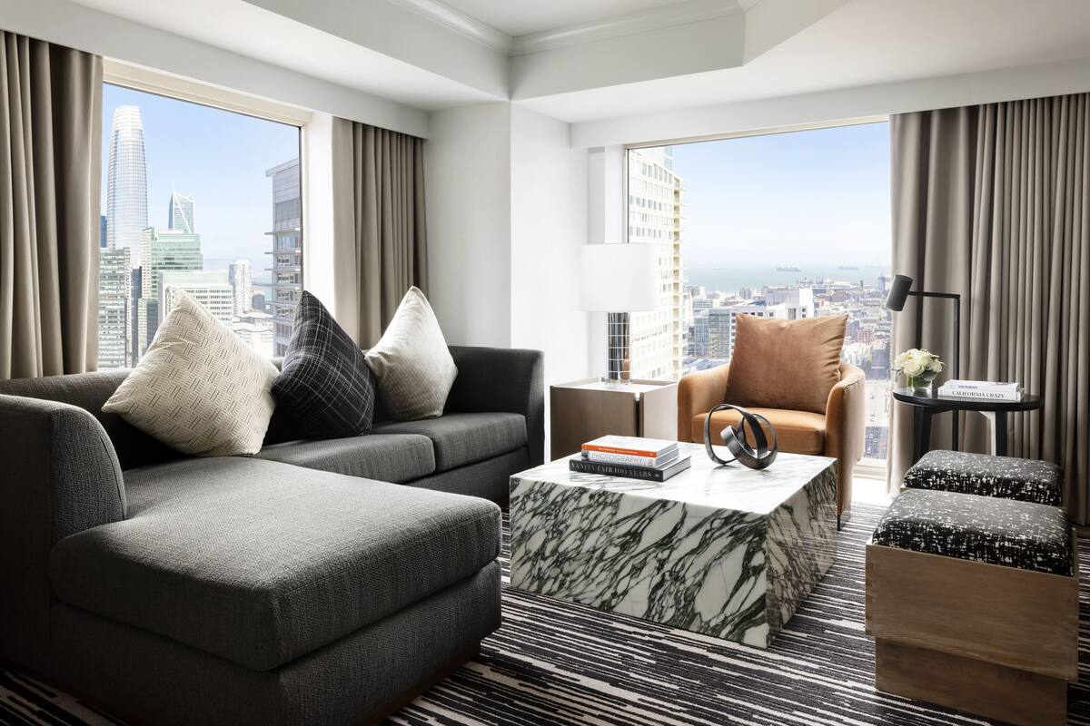 A modern hotel room with a grey sofa, a brown armchair, and a marble coffee table.