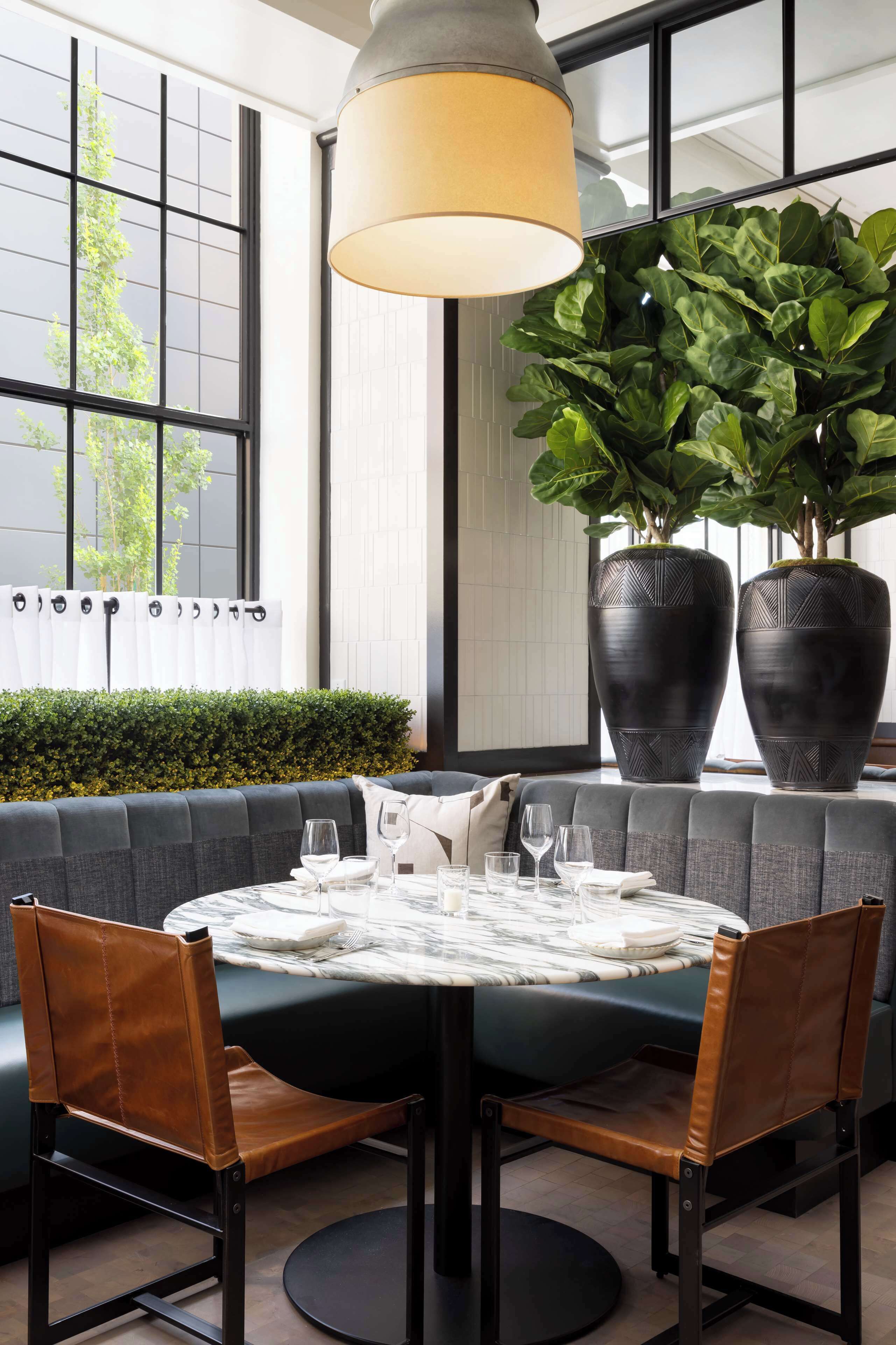 Un coin repas comprenant une table ronde, deux chaises, un canapé et une grande plante en pot.