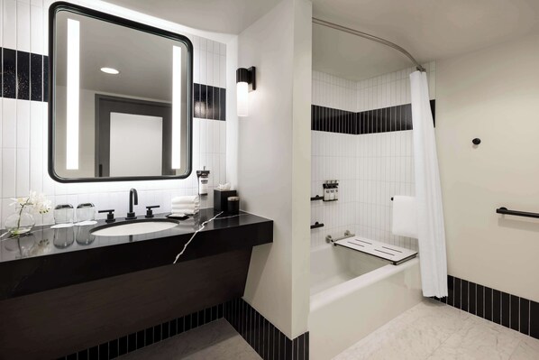 Un baño moderno con lavamanos de encimera negra, un espejo grande, una bañera y una cortina de ducha.