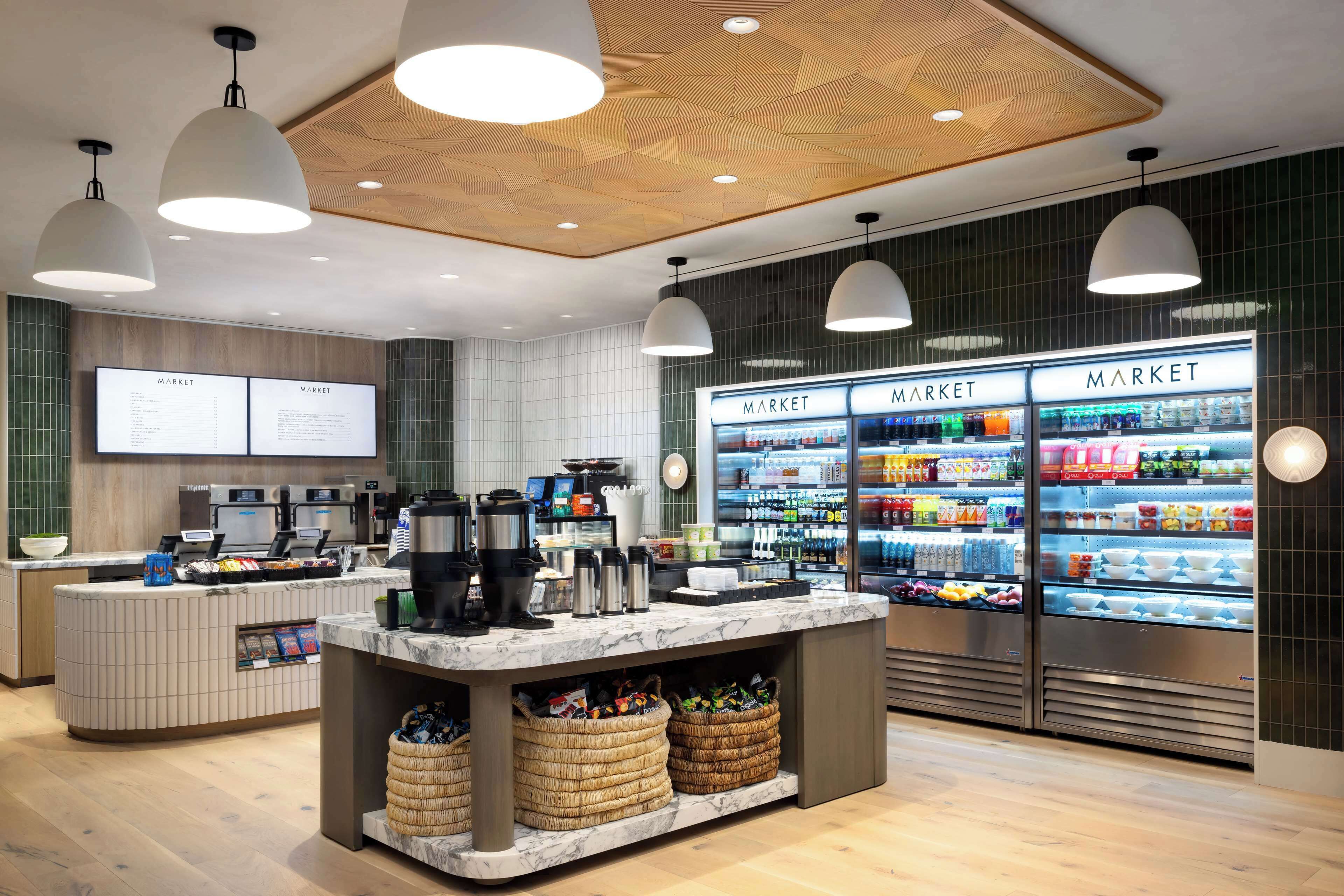 Un espacio comercial moderno con mostrador de mármol, máquinas de café y secciones refrigeradas identificadas como 