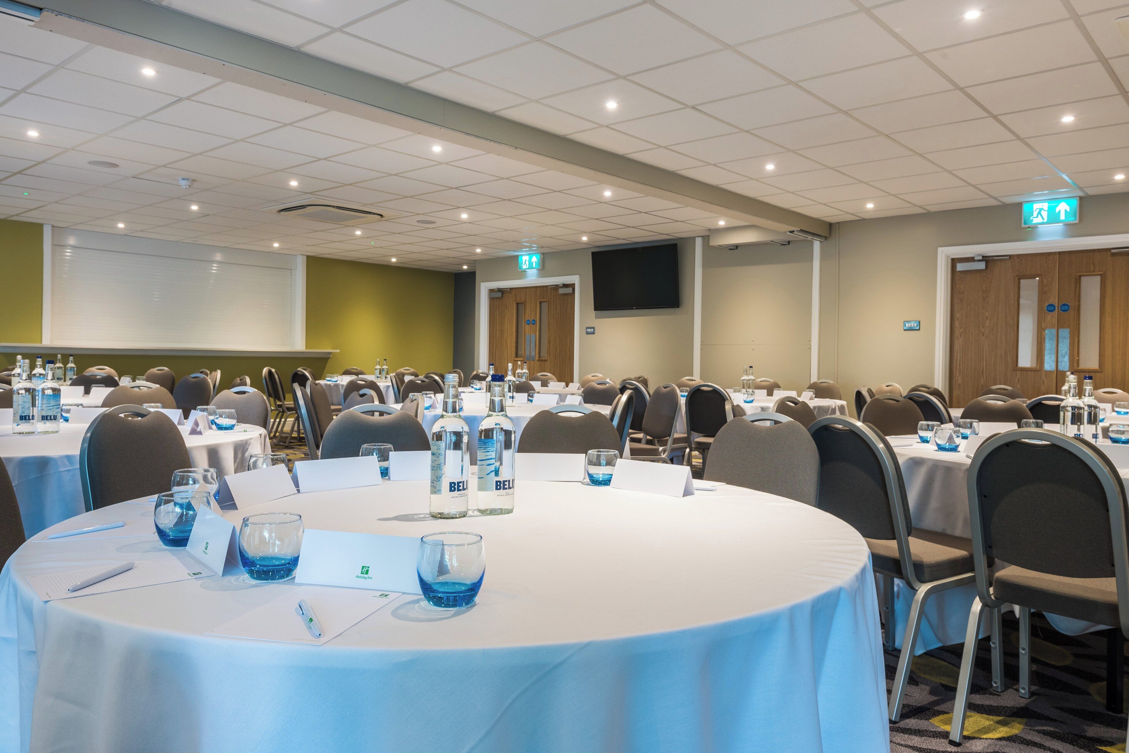 A conference room with round tables, chairs, nameplates, and water bottles.