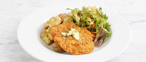 En tallerken med en paneret schnitzel, kogte kartofler og en blandet grøn salat.