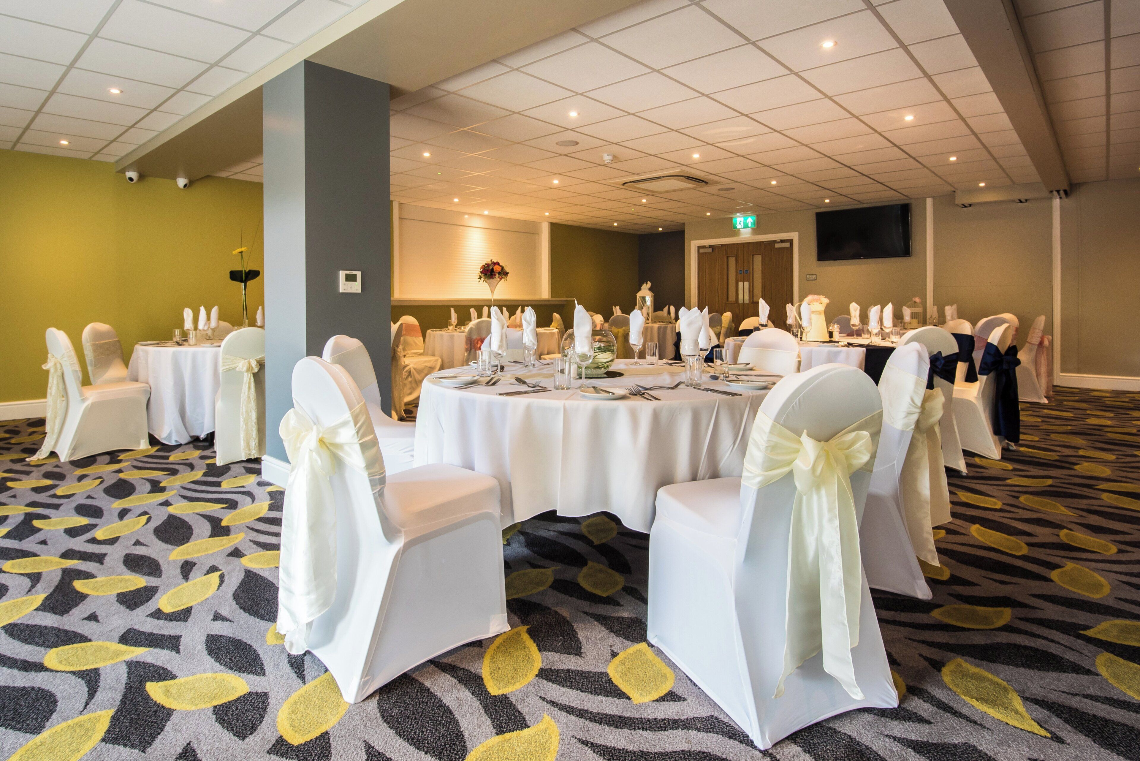 A conference room with round tables, white chairs with bows, and a patterned carpet.
