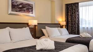 A hotel room with two beds, each with a dark gray bedspread and white pillows. There is a framed abstract painting on the wall above the beds, and a window with patterned curtains to the right. - Holiday Inn Lancaster by IHG (Lancaster)