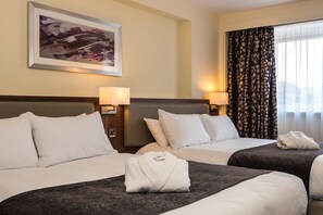 Une chambre d’hôtel avec deux lits, chacun recouvert d’une couvre-lit gris foncé et agrémenté d’oreillers blancs. Un tableau abstrait encadré est accroché au mur au-dessus des lits, et une fenêtre avec des rideaux à motifs se trouve sur le côté droit.