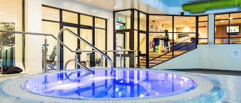 An indoor swimming pool with a glass barrier, a metal staircase, and a visible exit sign.