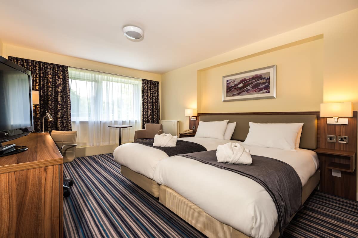 A hotel room with a large bed, a desk with a computer, a chair, and a TV.