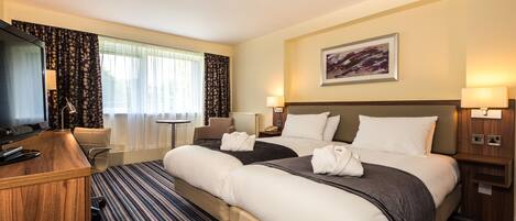 A hotel room with a large bed, a desk with a computer, a chair, and a TV.