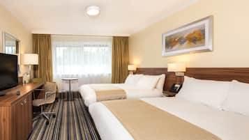 Een hotelkamer met twee bedden, een bureau met een televisie, een stoel, een klein tafeltje en een schilderij aan de muur.