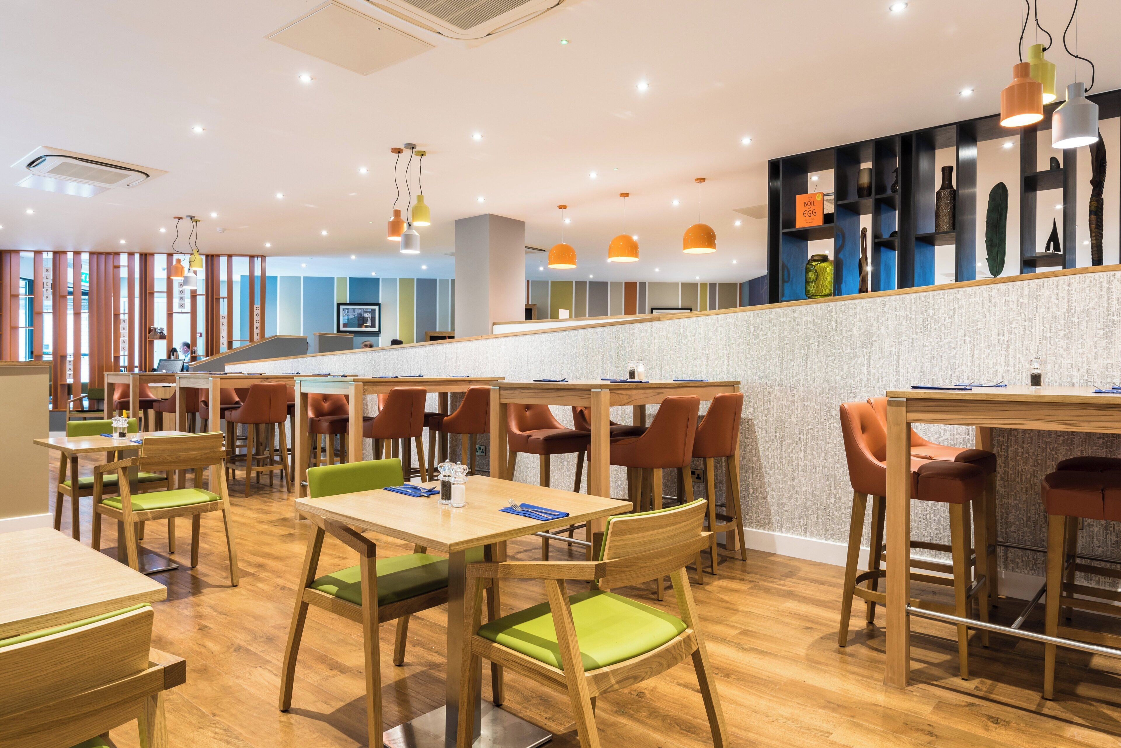 Ein modernes Restaurant mit Holztischen und -stühlen, einer Bar und verschiedenen Pendelleuchten.