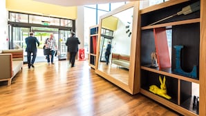 A lobby with wooden flooring, a sofa, a mirror, and a bookshelf with various items. - Holiday Inn Lancaster by IHG (Lancaster)
