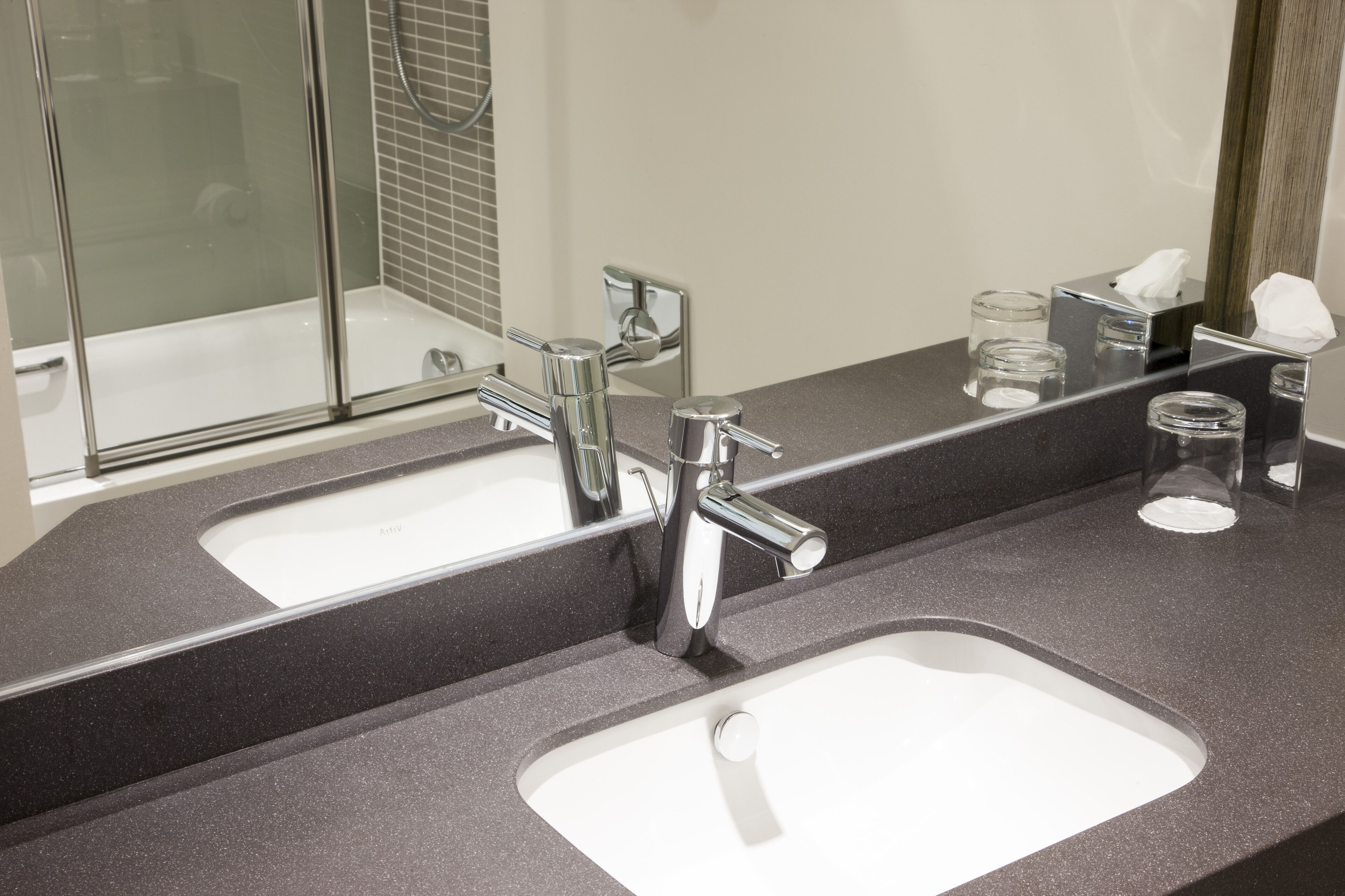 A modern bathroom with two sinks, a large mirror, and a glass shower enclosure.