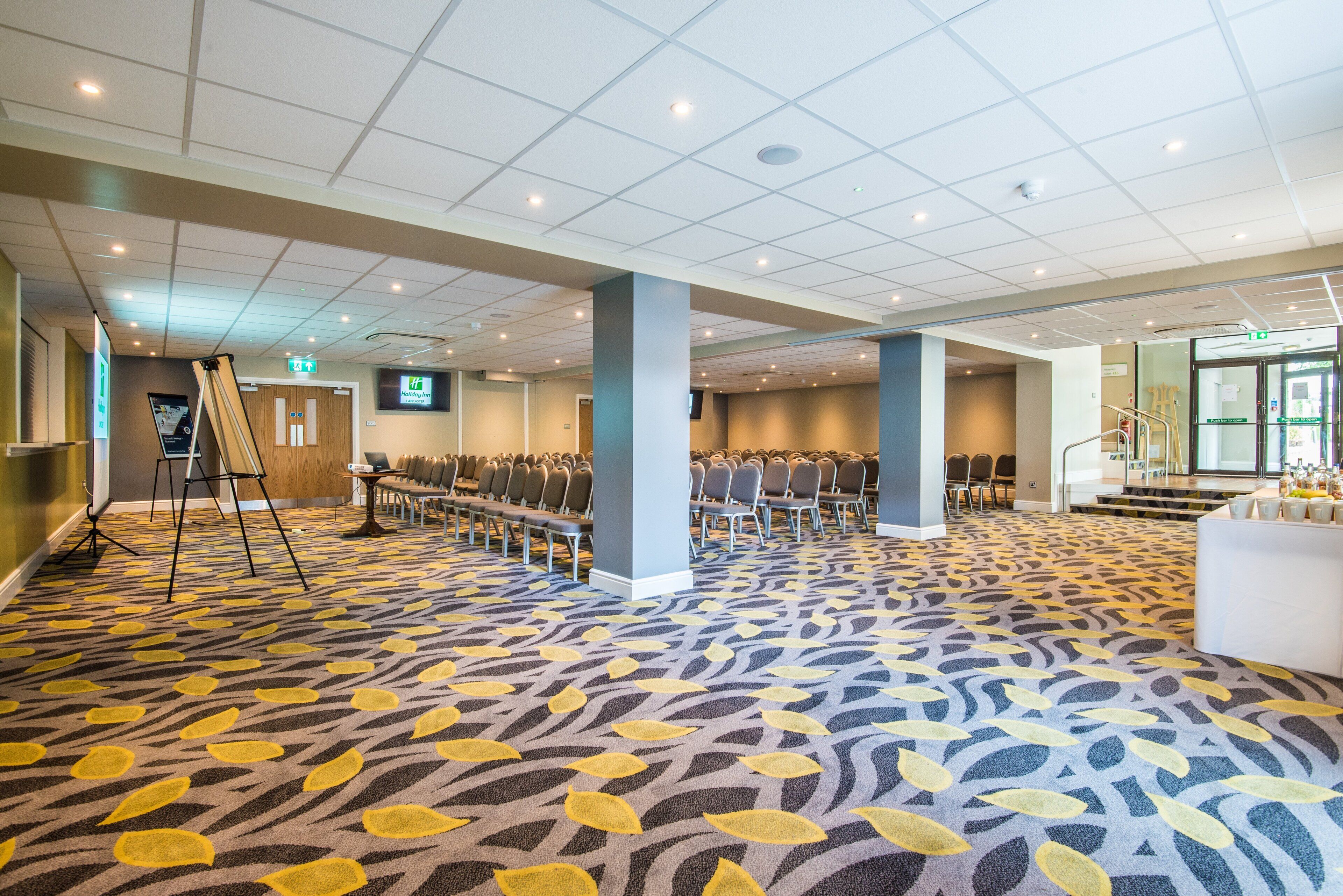 Un grand hall doté de rangées de chaises, d’une scène et d’un tapis à motifs.