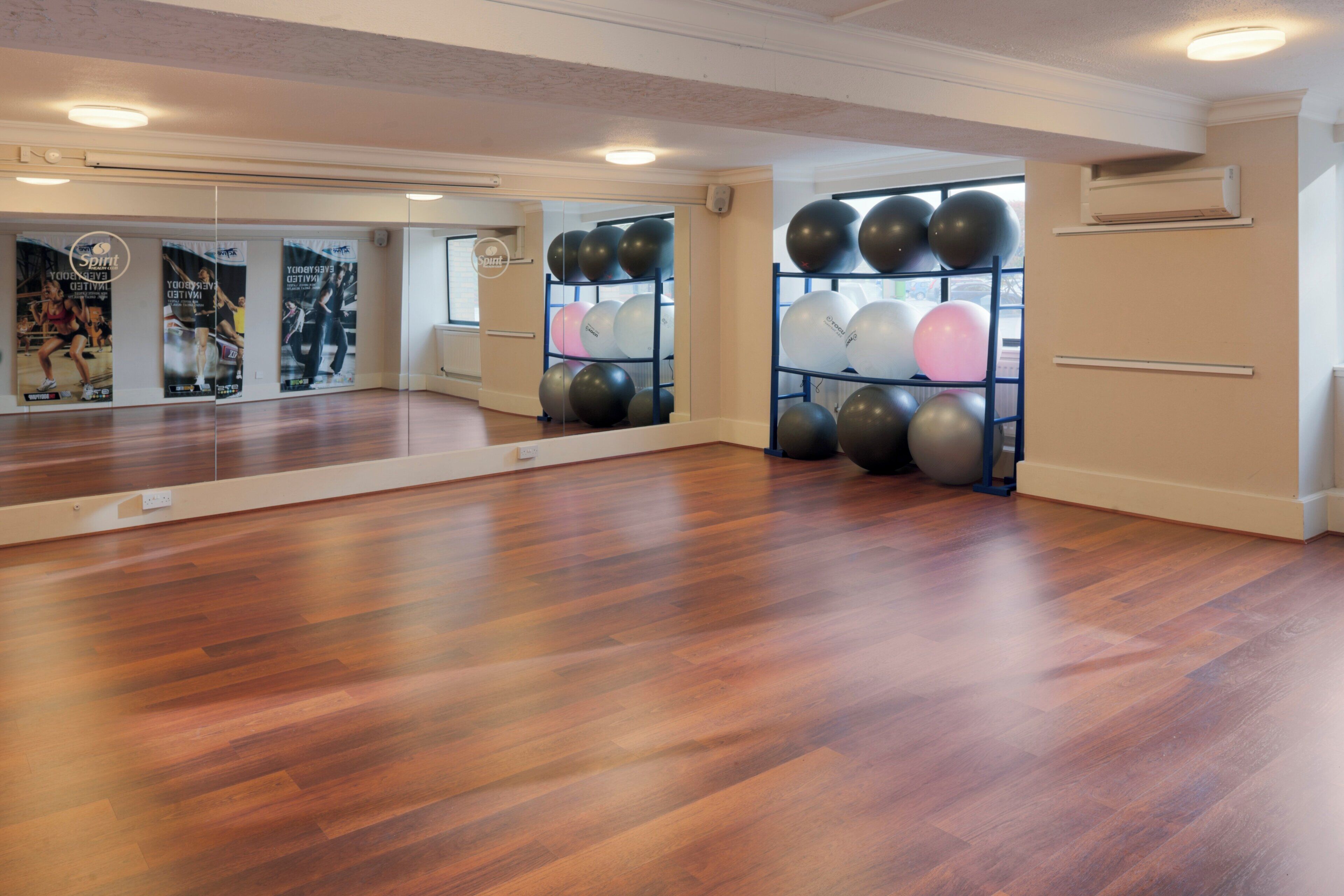 A spacious room with a wooden floor, a large mirror, and a wall-mounted shelf with exercise balls.