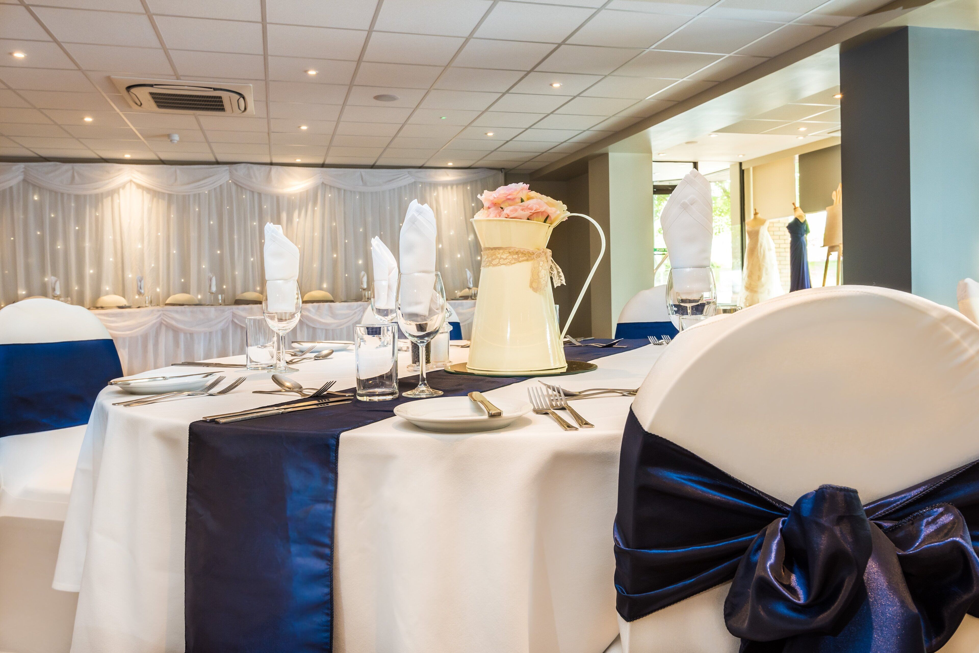 Een feestzaal met ronde tafels, gedekt voor een formeel evenement, inclusief witte tafellakens, bestek en glazen.