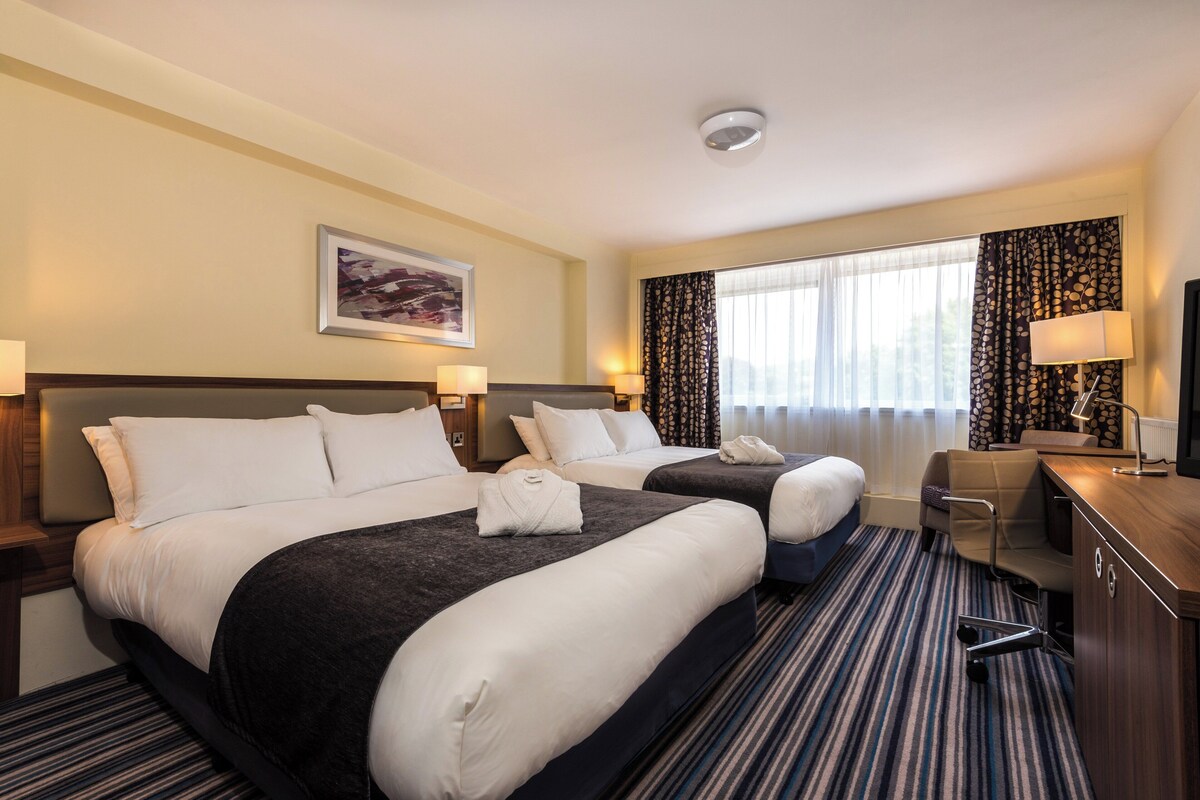 A hotel room with two beds, a desk, a chair, a television, and a window with curtains.