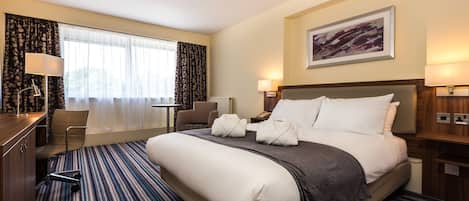 A hotel room with a large bed, a desk, a chair, and a window with curtains.