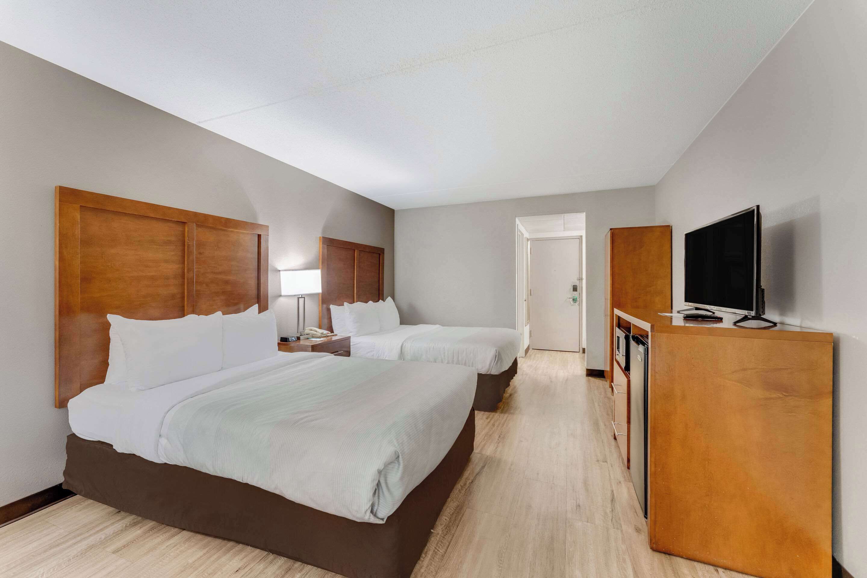 Una habitación de hotel con dos camas, un cabecero de madera, un televisor sobre un mueble de madera y una puerta que da a un baño.