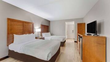 Una habitación de hotel con dos camas, un cabecero de madera, un televisor sobre un mueble de madera y una puerta que da a un baño.