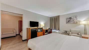 A hotel room with a large bed, a desk with a computer, a television, and a seating area with chairs.