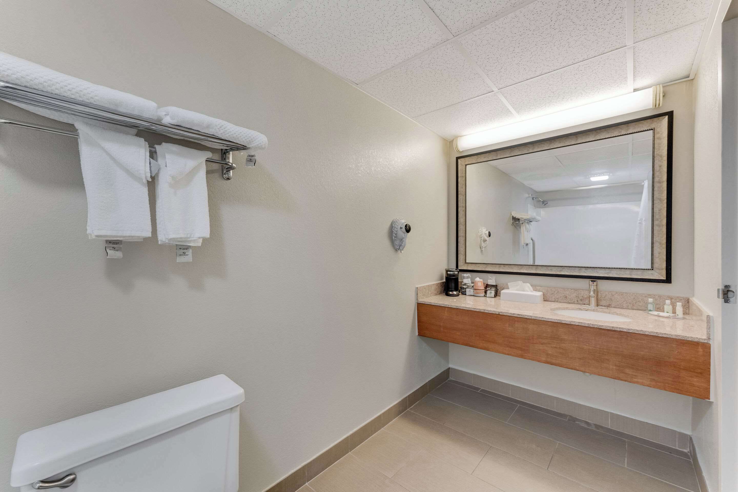 A bathroom with a toilet, a towel rack with towels, a sink with a mirror, and toiletries.