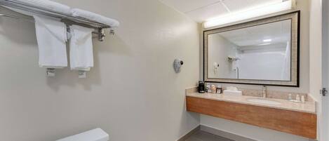 A bathroom with a toilet, a towel rack with towels, a sink with a mirror, and toiletries.