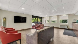 A spacious lobby with a modern design, featuring a seating area with red chairs and a grey sofa, a flat-screen TV mounted on the wall, and large windows providing natural light. - Quality Inn Easton (Easton)