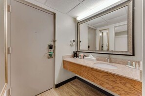 A hotel bathroom with a wooden vanity, a large mirror, and a hand sanitizer dispenser.