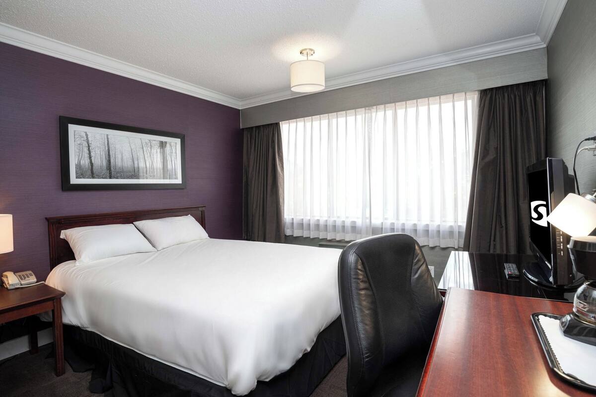 Een hotelkamer met een groot bed, een bureau met lamp, een stoel, een televisie en een raam met gordijnen.