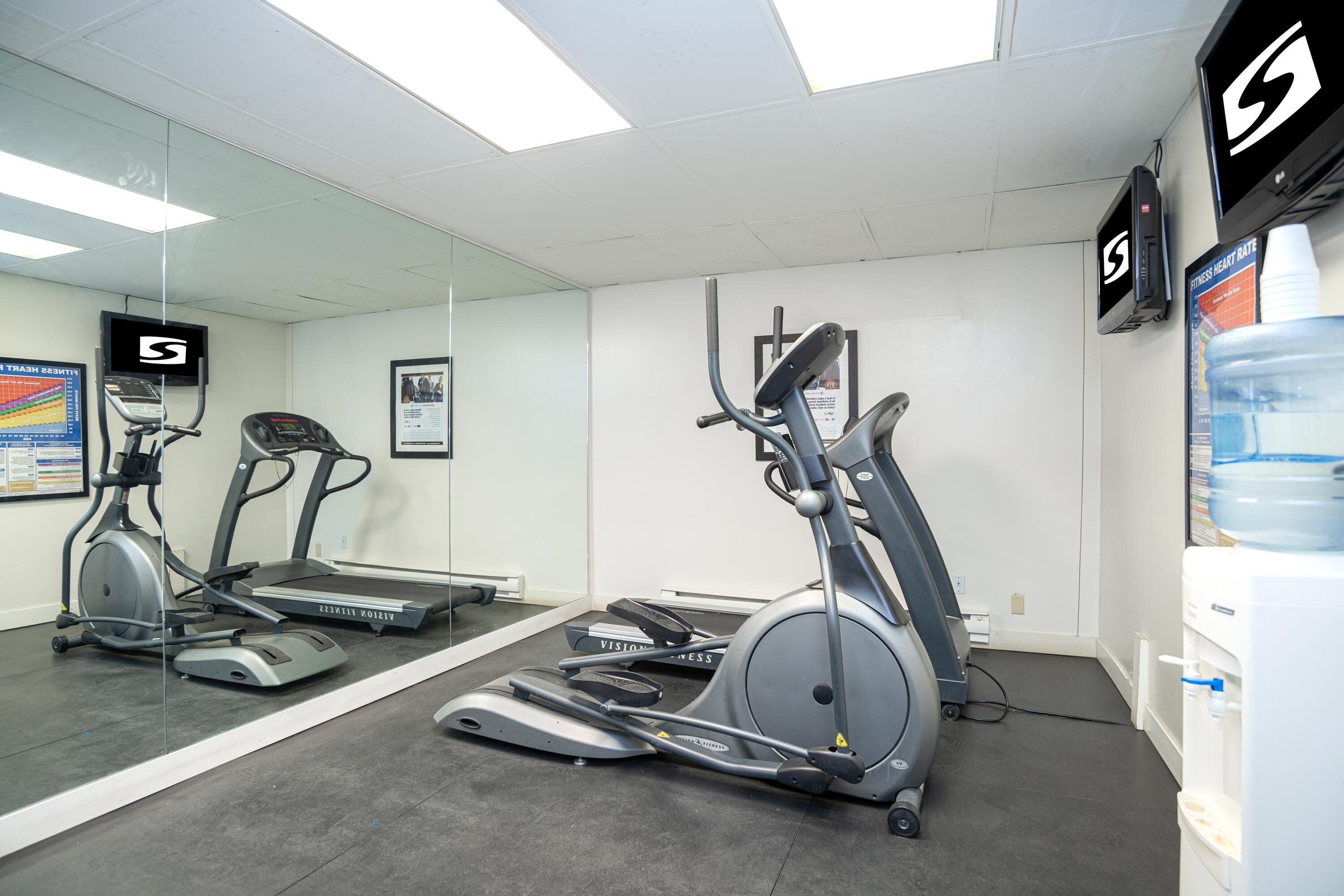 Ein Fitnessstudio mit Laufbändern, Crosstrainern und einem Wasserspender.