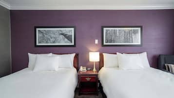 Una camera d'albergo con due letti, un comodino con una lampada e due quadri appesi al muro.
