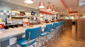 Un restaurant avec un comptoir, des tabourets de bar bleus et un panneau affichant le menu.
