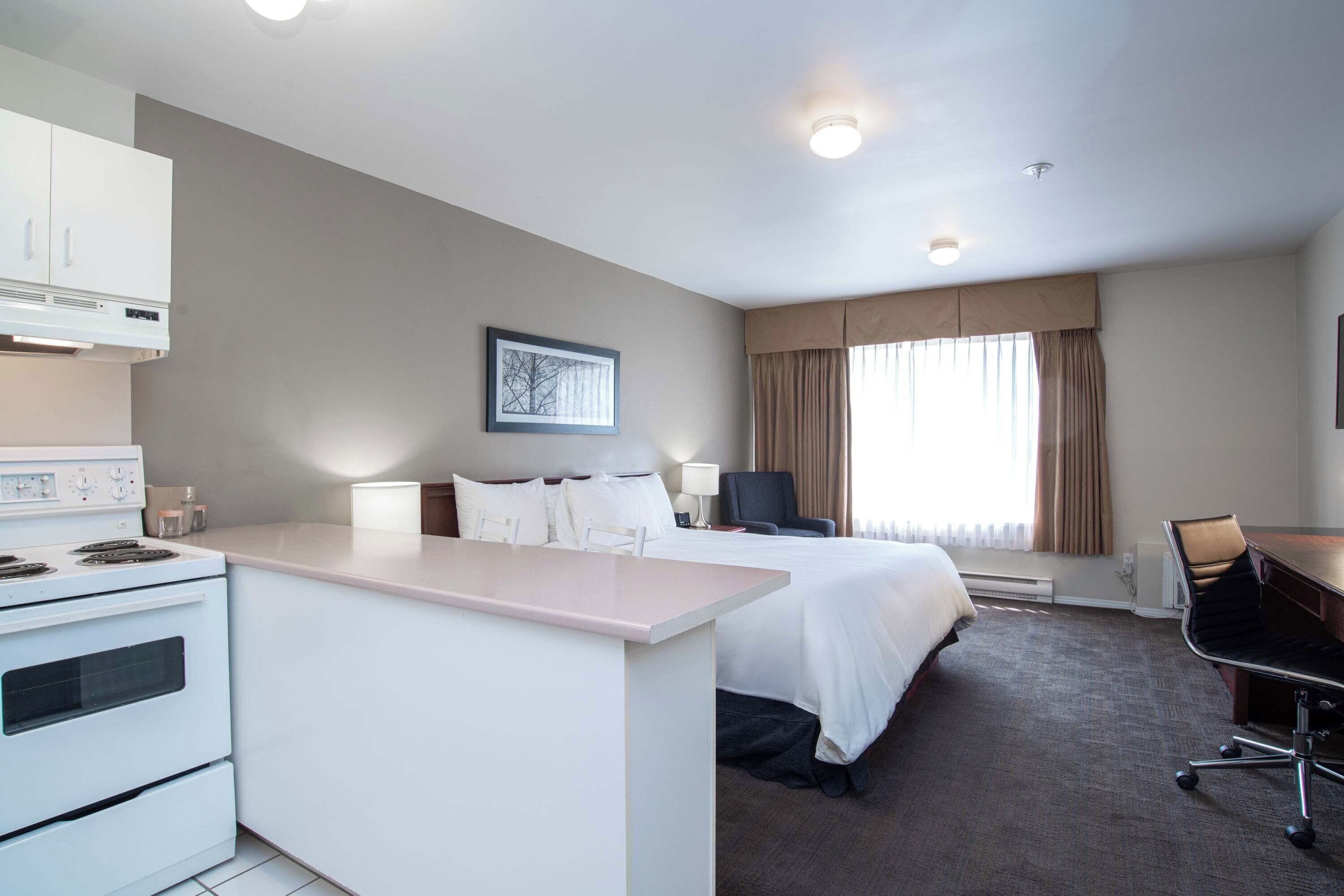 Una habitación de hotel con kitchenette, cama, escritorio y silla.