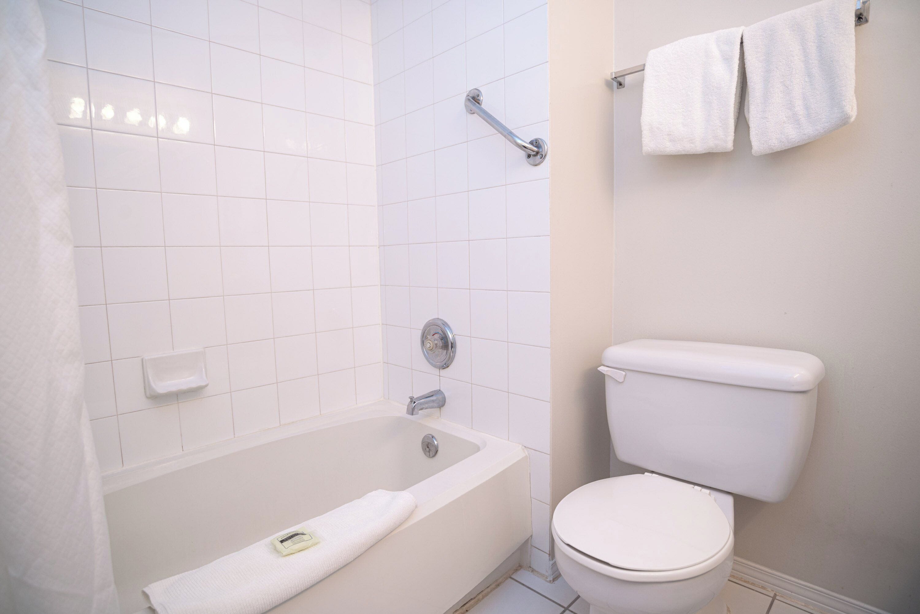 A bathroom with a bathtub, toilet, and a towel rack with two towels.