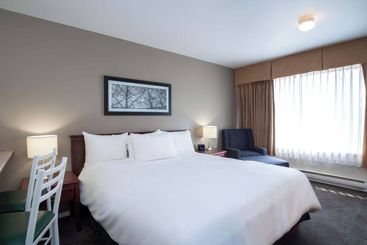 Hotelkamer met een groot bed, twee nachtkastjes, een stoel, een bureau, een lamp en een raam met gordijnen.