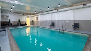 Une piscine intérieure à l’eau claire, entourée d’espaces de détente et dotée d’un plafond bien éclairé.