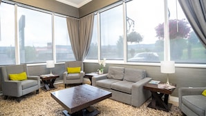 Un salon moderne comprenant un ensemble de canapés, une table basse et deux tables d’appoint avec des lampes. De grandes fenêtres offrent une vue sur l’extérieur.
